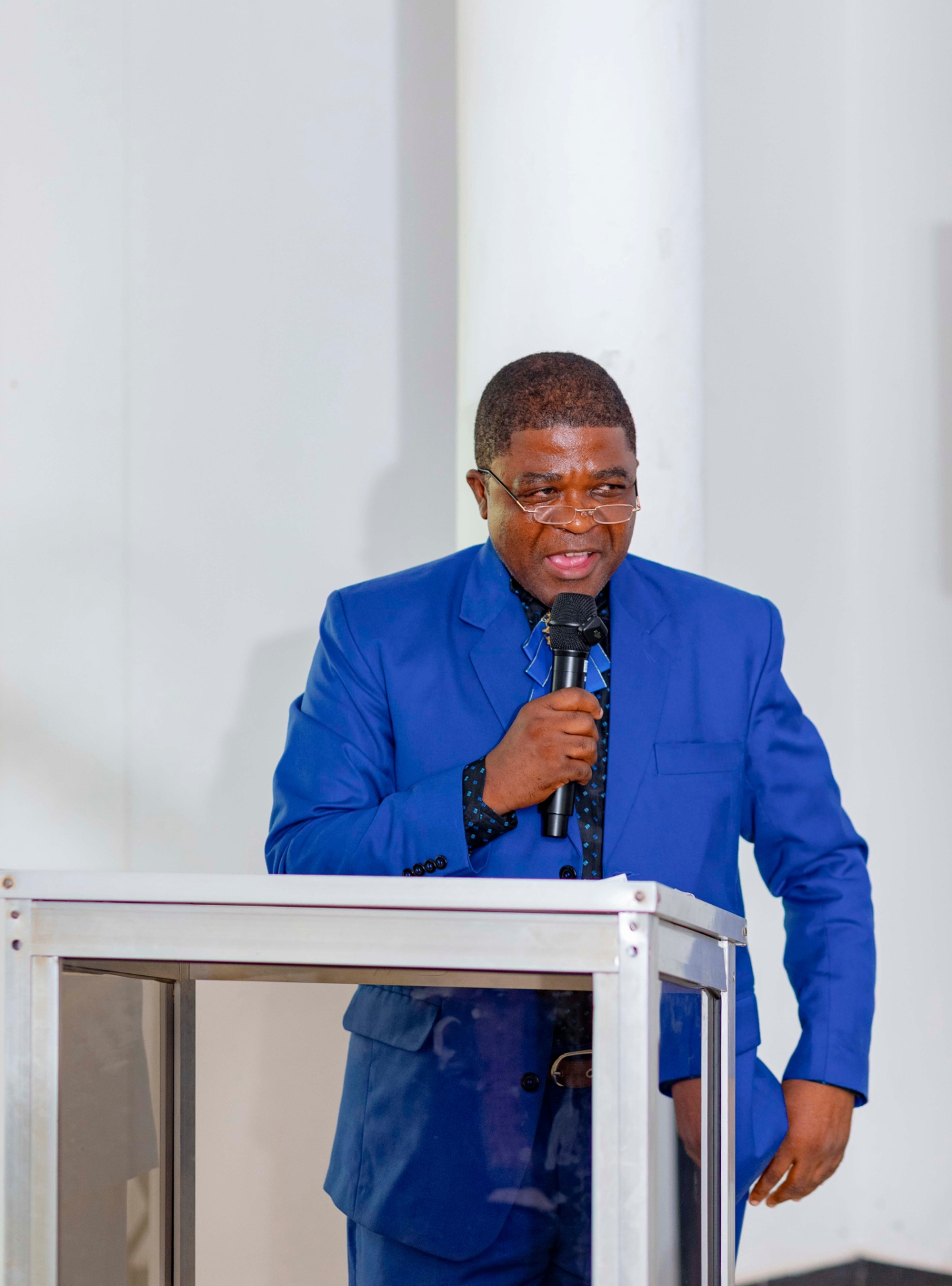Conference facilitator in a blue suit speaking at the podium during the GRA Inaugural Colloquium