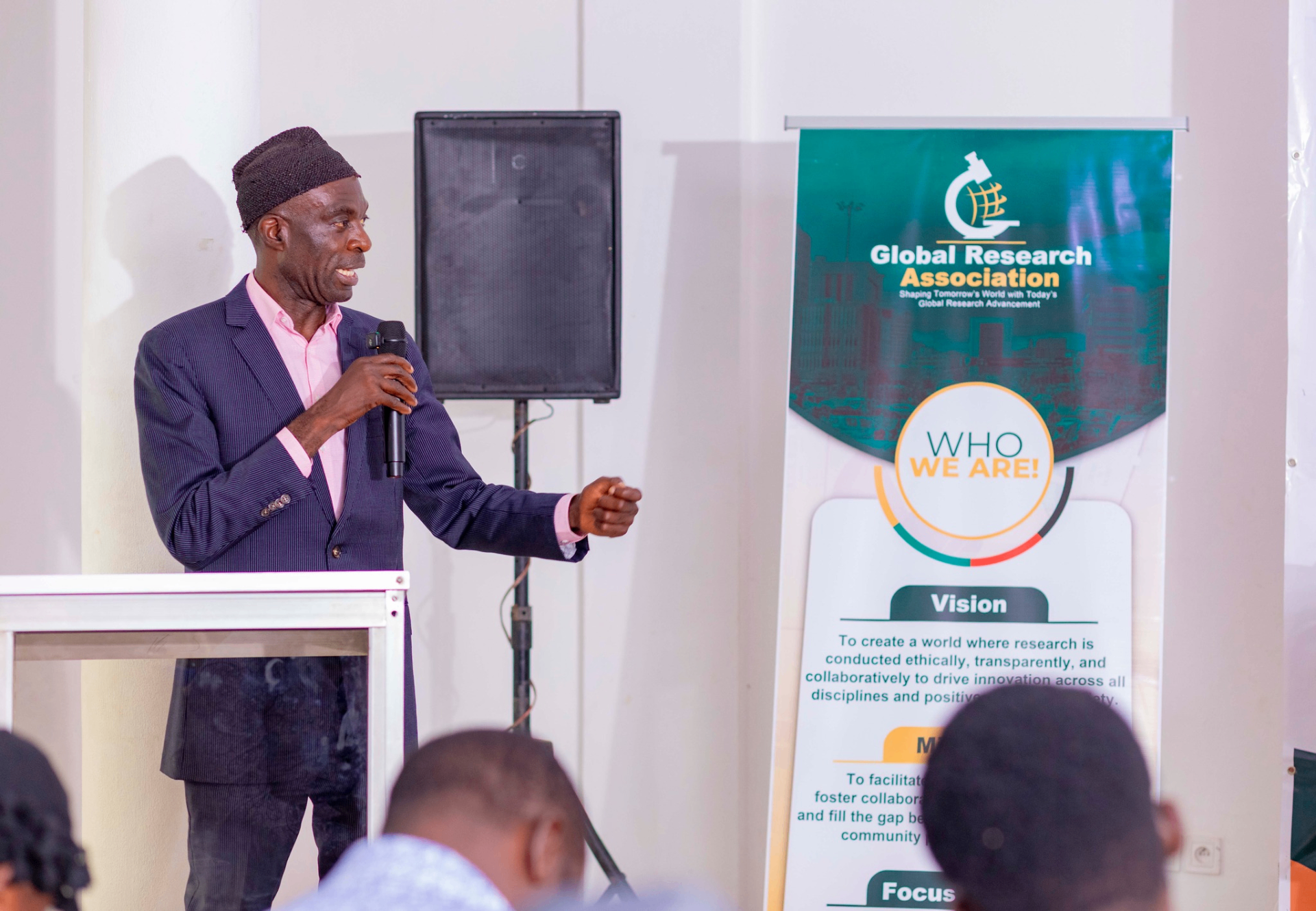 Conference facilitator speaking beside a GRA banner during the GRA Inaugural Colloquium