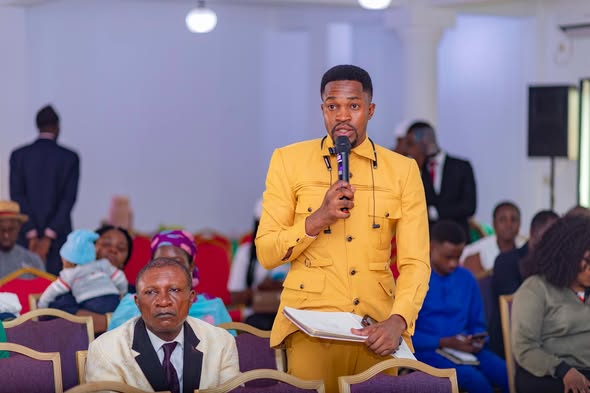 Colloquium participant in a yellow suit standing with a microphone and notes during a Q&A session at the GRA Inaugural Colloquium