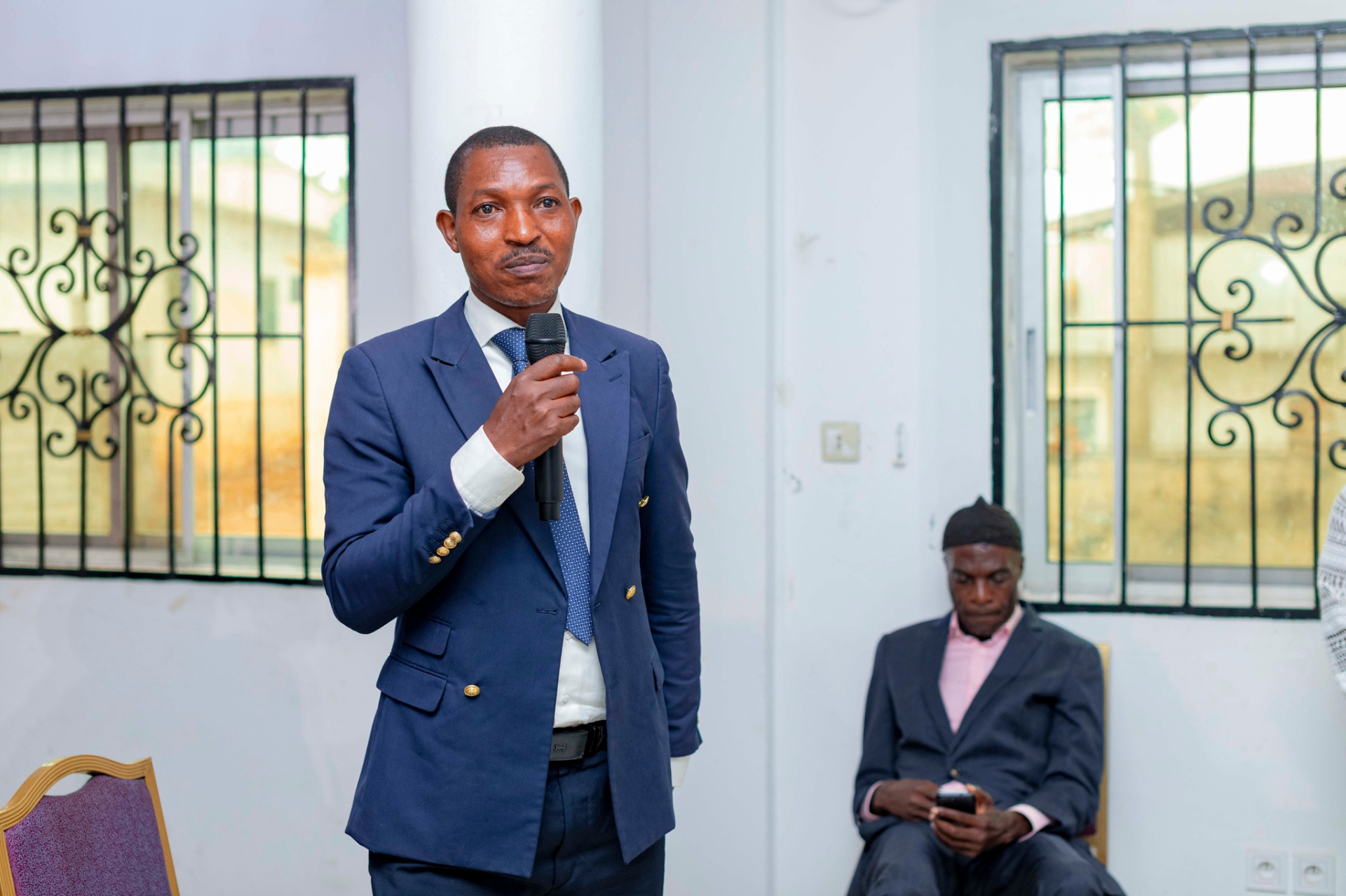 Colloquium participant in a navy blazer addressing the room with a microphone during a Q&A session at the GRA Inaugural Colloquium
