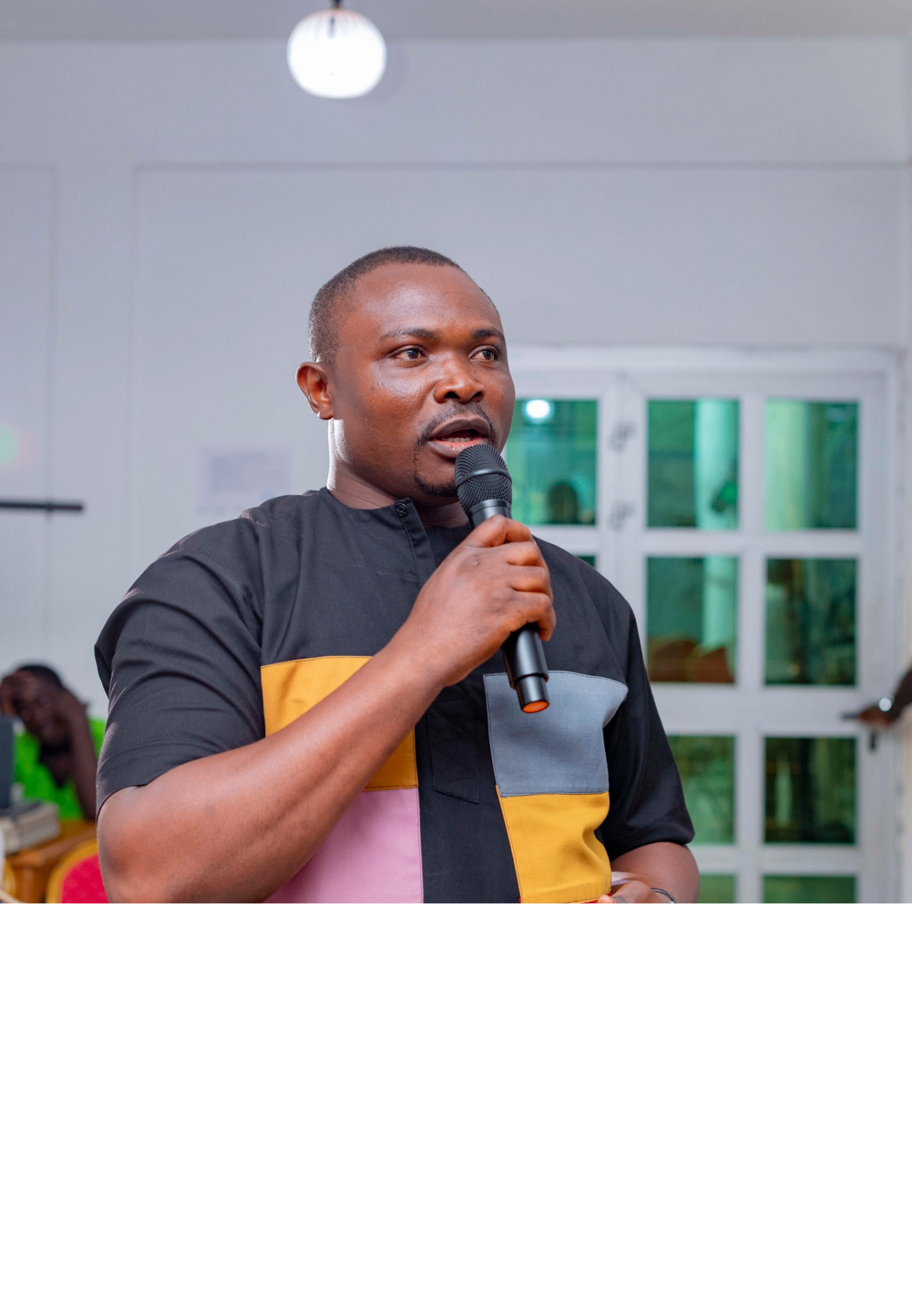 Colloquium participant in a black, mustard and grey patterned shirt speaking with a microphone during a Q&A session at the GRA Inaugural Colloquium