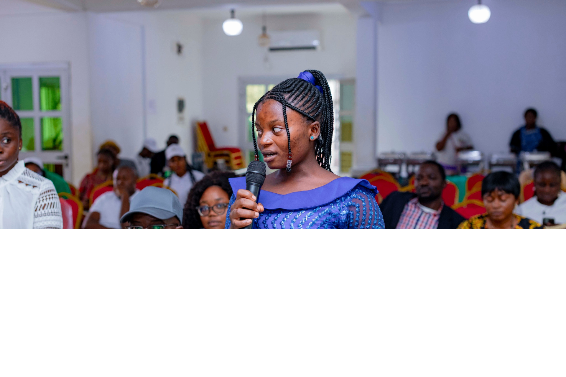 Young colloquium participant in a blue dress asking a question with a microphone during a Q&A session at the GRA Inaugural Colloquium
