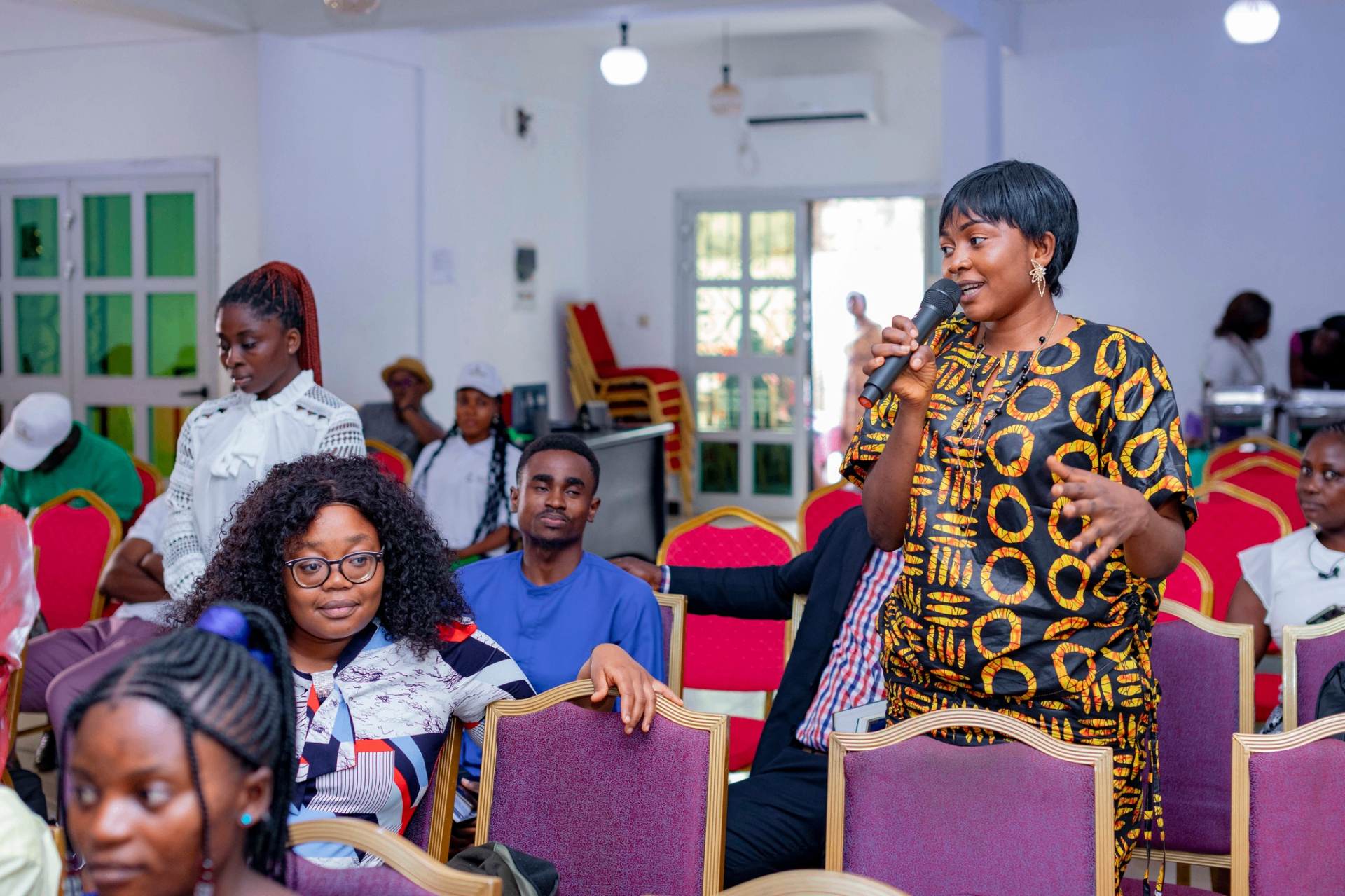 Colloquium participant in patterned attire speaking with a microphone during a Q&A session at the GRA Inaugural Colloquium