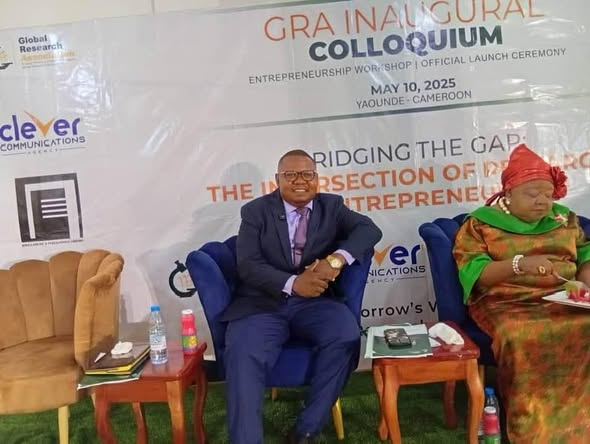 GRA Executive Director seated on stage beside the GRA Inaugural Colloquium backdrop in Yaoundé