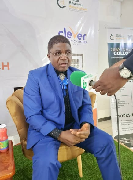 GRA guest in a blue suit responding to a press interview beside the GRA Inaugural Colloquium banner